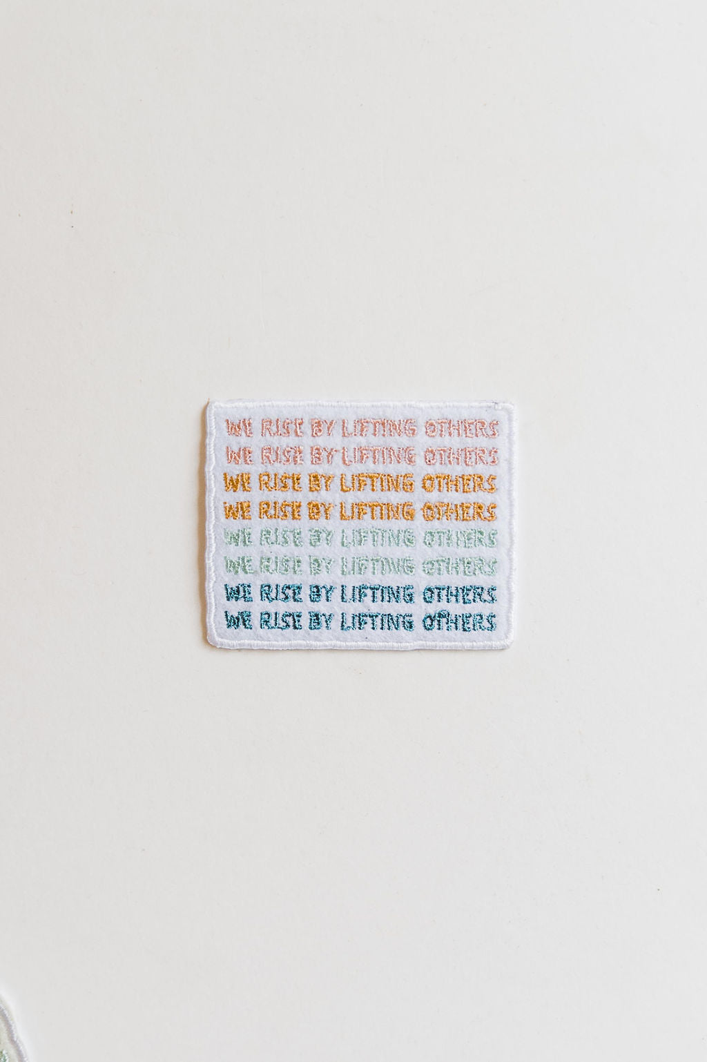 the design: we rise by lifting others the color: teal, light blue, mustard, and pink approx. 2" x 3.5" To apply: Each patch is woven with an iron on backing.   Ramble & Co. is a family owned business. Shop at shop.rambleandcompany.com or visit our store in Wichita Falls, Texas || small batch/ hand printed tees + fine art prints | your source of encouragement + inspiration.