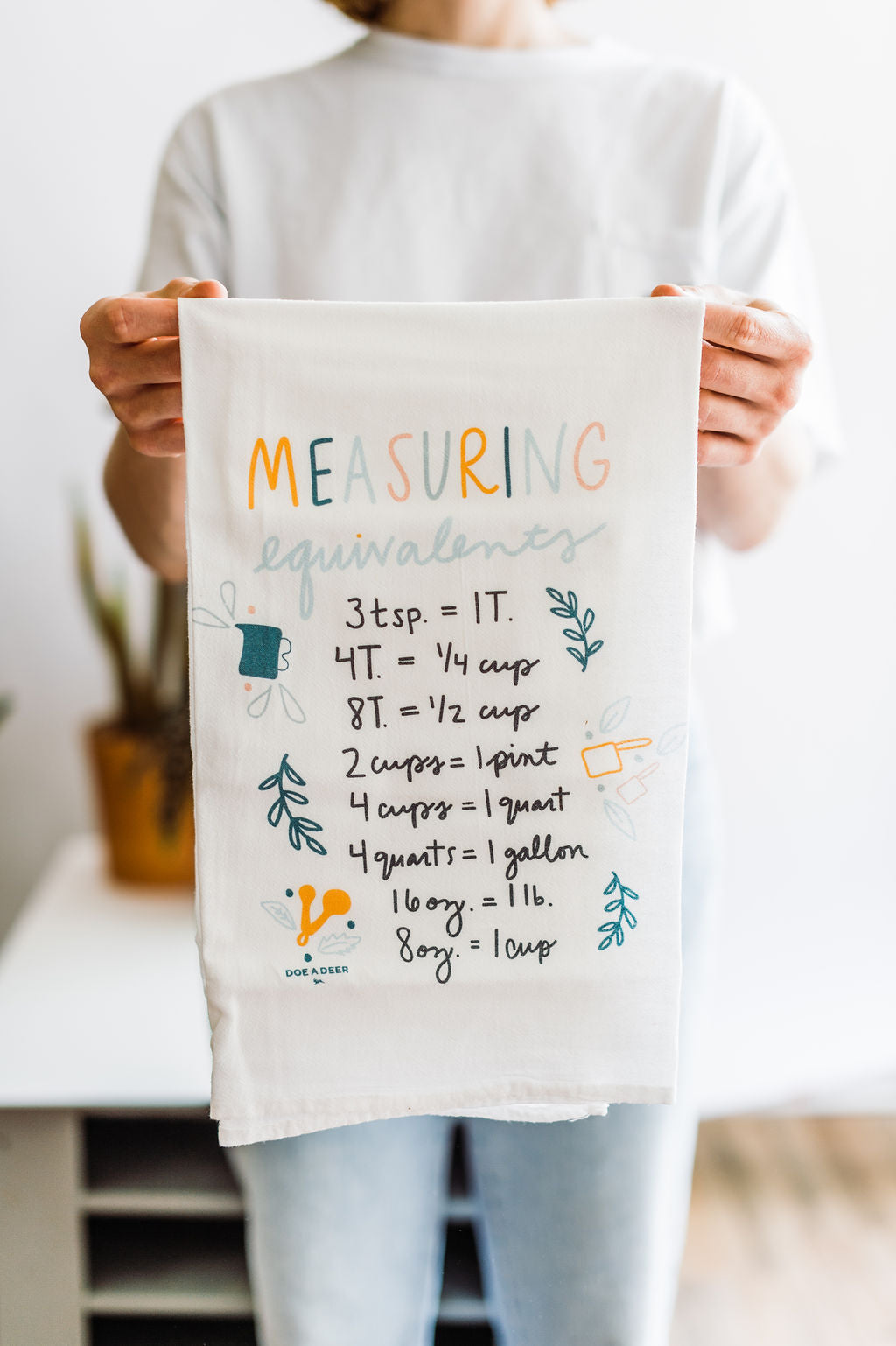 White flour sack towel with measuring equivalents in a 5 color design by Doe a Deer Designs || you can shop now at  shop.rambleandcompany.com or visit our storefront in downtown Wichita Falls, Texas || small batch + hand printed tees | home goods | paper goods | gifts + more